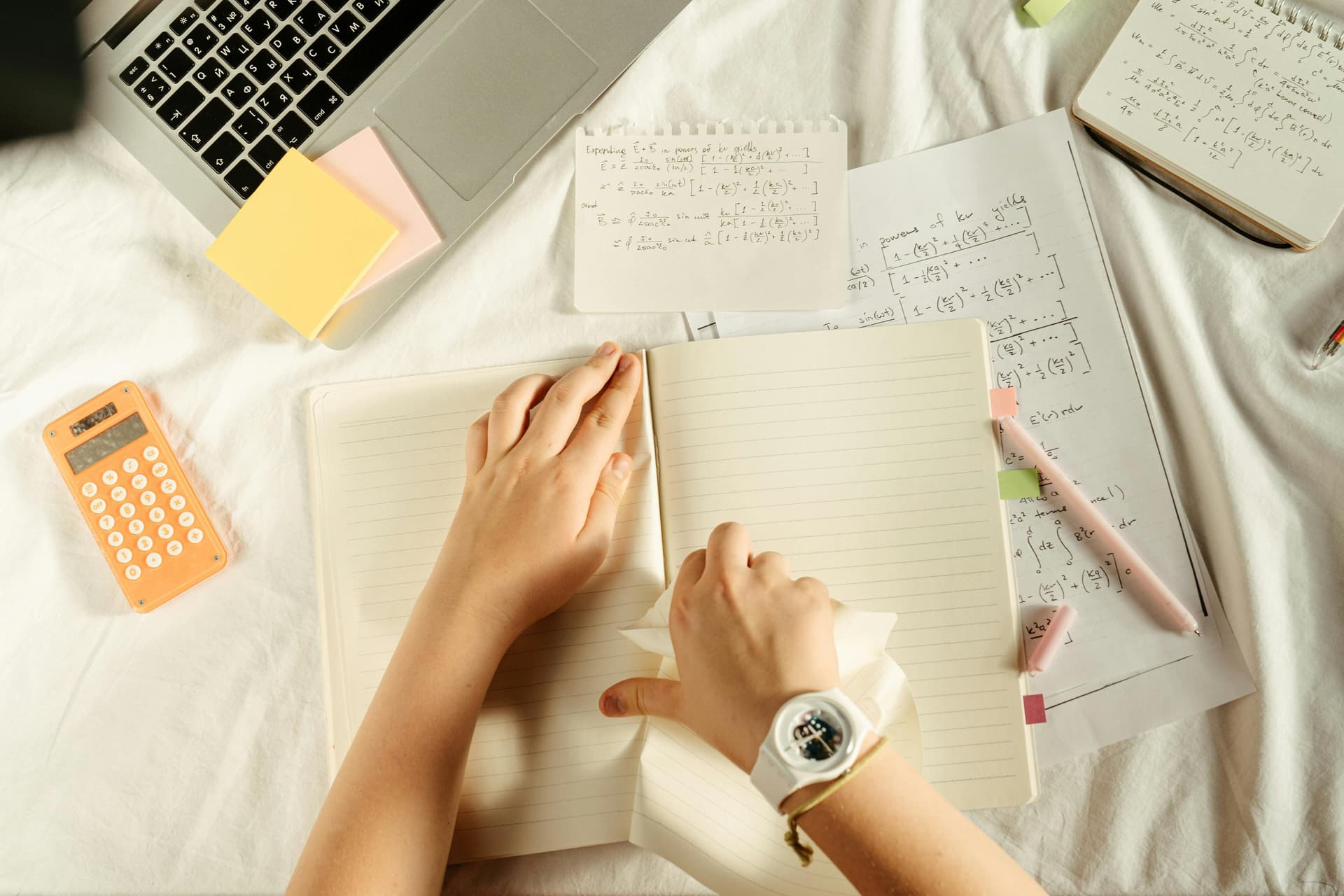 Student study setup with notebook, equations, calculator and laptop