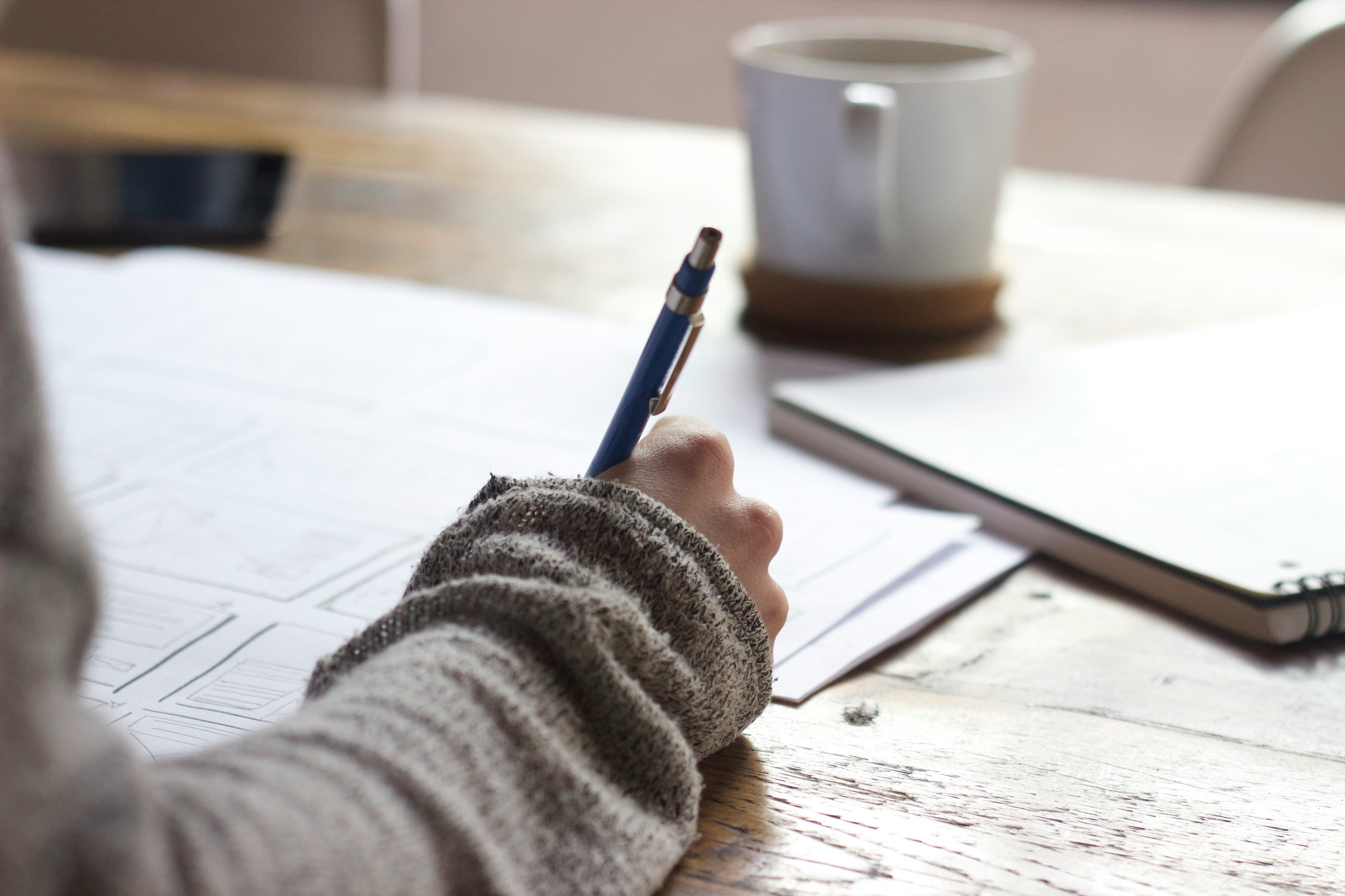 Student writing notes with pen and coffee nearby